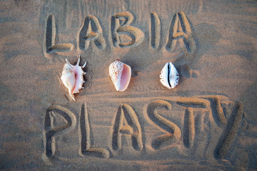 labiaplasty written in sand on beach with shells