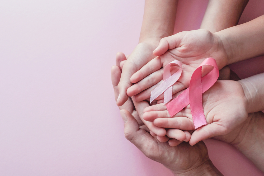 Three sets of women's hands holding breast cancer ribbons.