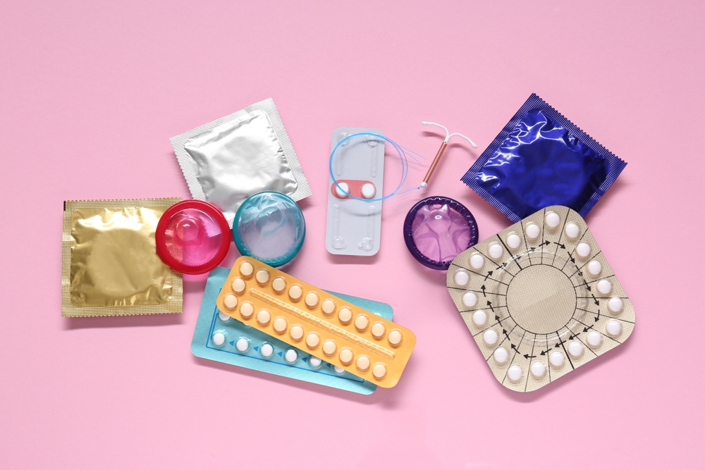 Contraceptive pills, condoms and intrauterine device on pink background.